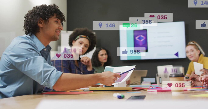 Discussing office-attired team reviewing documents on table in meeting room with social media icons