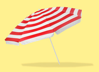 Red striped beach umbrella casting shadow on yellow background