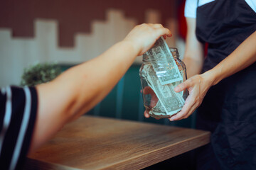 Customer Puts Money in the Tip Jar in a Restaurant. Person contributes generously to round out the...