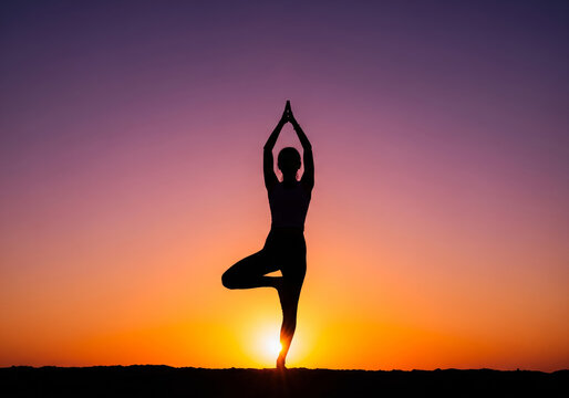 Silhouette of a woman in a yoga tree pose at sunset