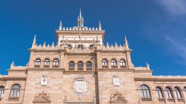 Timelapse of the Cavalry Academy facade in Plaza de Zorrilla, Valladolid, Spain. Historic military building with intricate architecture, surrounded by a busy urban scene under a blue sky with clouds.