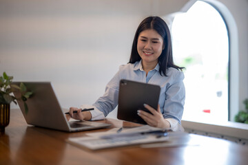 woman is sitting at a desk with a laptop and tablet in front of her