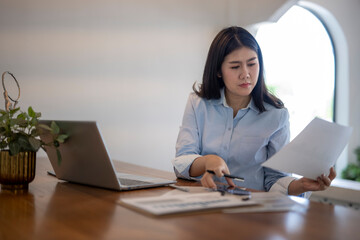 woman is sitting at a desk with a laptop and a stack of papers