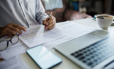 asian businessman holding pen reviewing document and business contract on desk in office using...