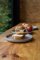 Simple breakfast setup on a wooden table includes toast with cheese, croissants, and apples. Natural light and forest views create a peaceful, rustic glamping atmosphere.


