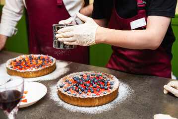 Dusting powdered sugar on berry fruit tart.