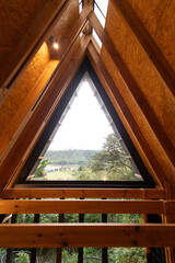 A triangular window crowns the peak of a glamping cabin roof. Viewed from above, the sharp lines...