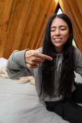 A smiling young woman relaxes comfortably on a cozy bed inside a rustic glamping tent, bathed in soft natural light, radiating warmth, happiness, and peacefulness.

