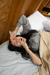 A young woman rises from bed, yawning and stretching with her hand on her forehead, bathed in soft morning light inside a warm and rustic glamping tent.

