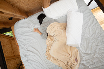 A young woman sleeps peacefully, wrapped in soft white sheets from the waist down, seen from above in a cozy glamping tent. A serene, intimate moment of rest.

