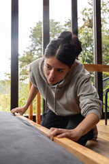 Close-up shot of a young woman’s hands smoothing out bed linens in a modern wooden cabin. The warm tones and natural light highlight a moment of care, presence, and simplicity during a quiet mountain 