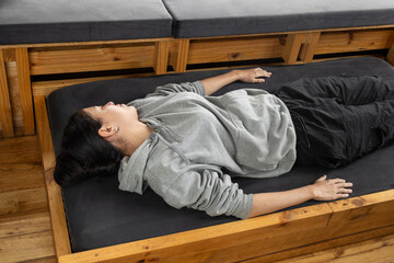 A serene young woman lies comfortably on her back atop a beautifully crafted wooden bed that slides out from a drawer inside a stylish glamping tent. This captivating image perfectly blends the allure