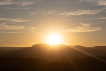 Sunset behind the mountains with golden rays and soft clouds, evoking tranquility and the beauty of nature at dusk.