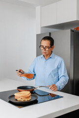 Senior man in blue shirt adds a freshly made pancake to a stack on a black plate. Homemade...