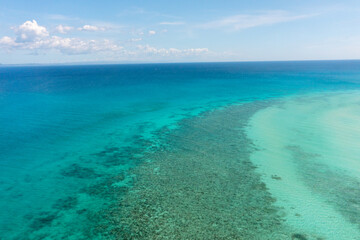 Tropical seascape with sea surface with corals and turquoise clear waters. Blue sky and clouds....