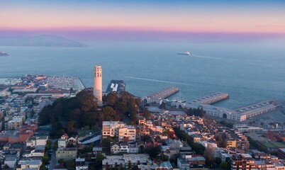 A high-angle view captures Coit Tower, a landmark in San Francisco, USA, at dawn. The image showcases the city's skyline, bay, and a ship sailing in the distance.