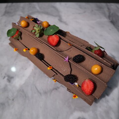 uncut chocolate roll cake topped with long chocolate chips and small fruits