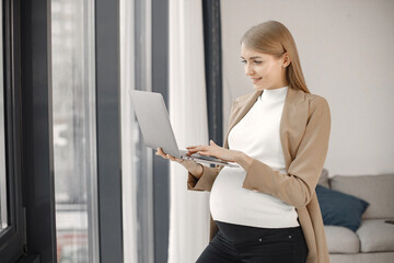 Pregnant lady typing on a laptop while standing in modern office