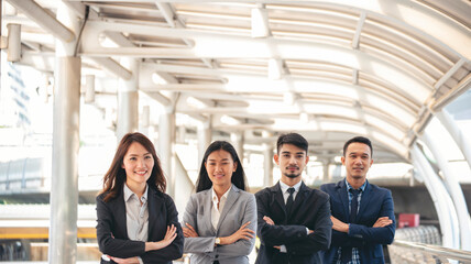 Obraz premium Portrait Group of businesspeople arms crossed smiling look at camera in modern city background. Happy Businessman, businesswoman teams partnership. Business people teams positive teamwork standing.