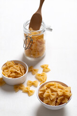 Raw farfalle pasta in a white bowl and glass jar on white background, Bow-tie shaped pasta...