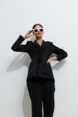 fashion woman in black outfit wears white sunglasses posing confidently against white background,...