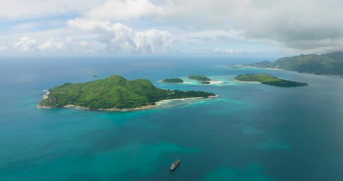 Small isolated islands with dense green vegetation surrounded by vibrant turquoise waters under a partly cloudy sky. Seychelles, Mahe. Ile au cerf island.