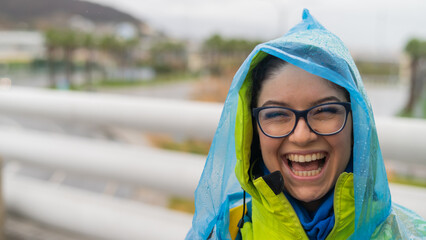 Portrait of a smiling woman with glasses wearing a raincoat outdoors.