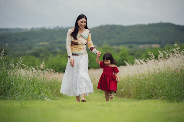 happy mother walking with her toddler girl on grass field