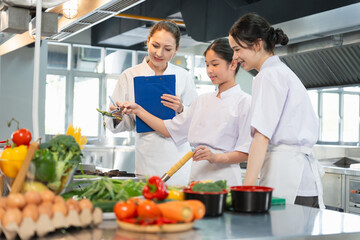 Young Chefs Learning to Cook with Fresh Ingredients, Culinary Instructor Guides Students in a Professional Kitchen, Women in Chef Uniforms Preparing Food in a Commercial Kitchen