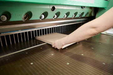 Precision cutting of a cardboard sheet stack using guillotine shears in a busy workshop filled with...