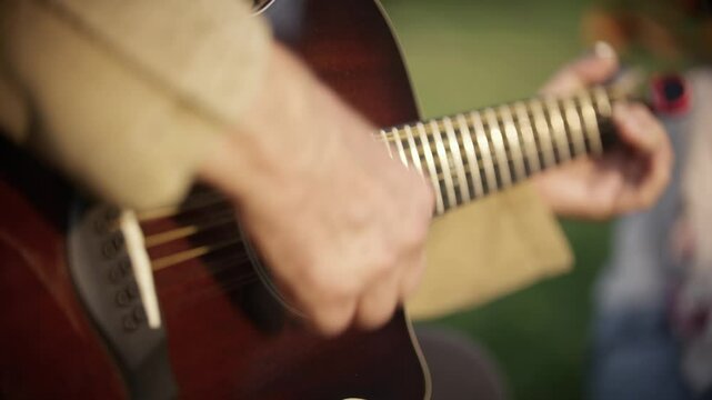A hobby guitarist plays on an acoustic guitar at a picnic in the park