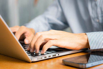 Person, hands and typing on laptop in office for email, spreadsheet and proposal or application for work. Man, online and technology with bokeh for task or drafting, writing notes and report.