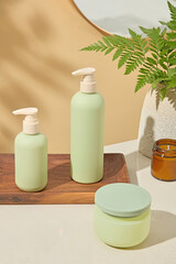 Pastel green bottles and body cream on wooden board with soft background and leaves. Natural light...