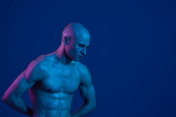 Athletic man posing confidently against a dark blue background, showcasing strong muscles and intriguing lighting. Perfect for fitness or health-related themes.