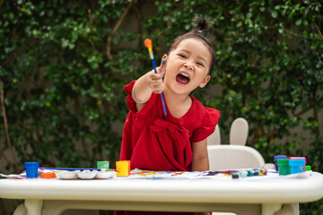 happy toddler girl painting watercolor in paper at backyard.