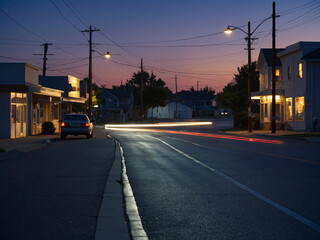 Out-of-focus suburban street corner with distant shop lights and soft vehicle light trails captured just after sunset with clear evening sky fading to deep blue, every source of light