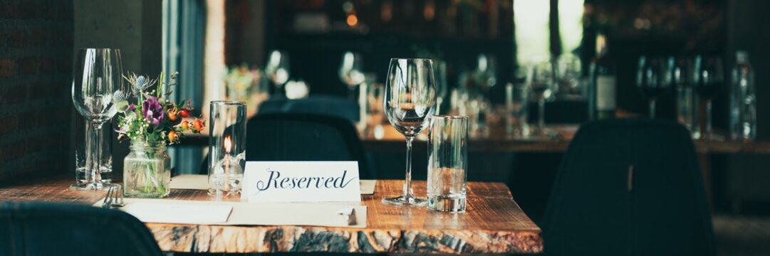 Cozy restaurant table with 'Reserved' sign, elegant glassware, and floral centerpiece. Inviting dining atmosphere with reserved seating and stylish decor. Restaurant's reservation sign on a table.