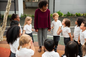 Teacher with diverse group of children outdoors. Kids in white uniforms. Engaged teacher, attentive...