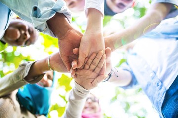 Diverse group of people joining hands in a circle, symbolizing teamwork and unity. Hands of different ethnicities and genders coming together in harmony. Happy students stacking hands in teamwork.