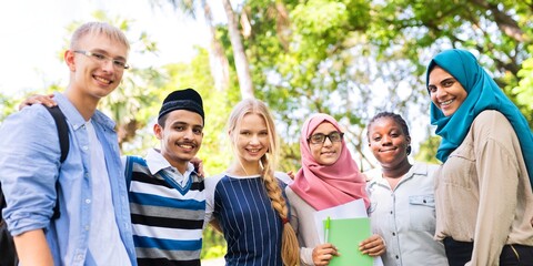 Diverse group of young adults smiling outdoors. Friends from various backgrounds, including women in hijabs. Multicultural youth bonding. International students and friends at schoolyard.