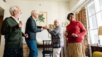 Group of seniors dancing indoors. Diverse elderly men and women, enjoying music at home. Seniors men and woman friends dancing at home. Diverse elderly friends dancing, have good time in cozy room.
