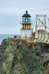 Dramatic coastal view of Point Bonita Lighthouse on a rocky cliff with a suspension bridge and powerful ocean waves, Marin Headlands, California