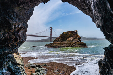 Dramatic view of the Golden Gate Bridge from a rocky cave at Kirby Cove Beach, San Francisco. Ocean...