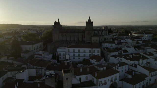 Drone flies toward cathedral with sunset to the left in Evora, Portugal