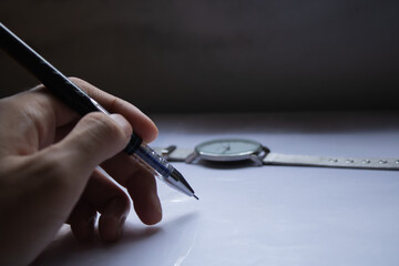 A hand holding a pen, about to write or sign on a white surface, with a watch in the background....