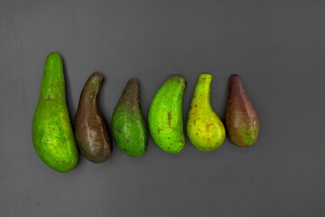 Six avocados, a healthy fruit packed with benefits, are lined up on the floor, some are raw and some are almost ripe.