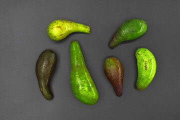 Six avocados, a healthy fruit packed with benefits, are lined up on the floor, some are raw and...