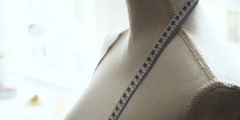 A tailor's mannequin with a measuring tape draped over it, symbolizing fashion design, sewing, and...
