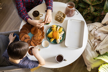 Children having breakfast with pancakes, fruits, and tea at round table with cozy cat, natural light
