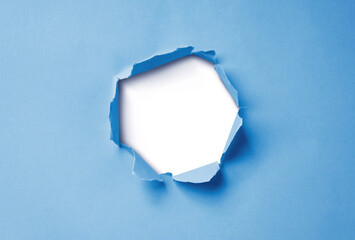 Close-up image of a blue paper sheet with a jagged hole torn through the center, revealing a transparent background.